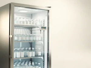 Geopende roestvrijstalen medische koelkast met farmaceutische injectieflacons op nette planken en temperatuursensor in klinische omgeving.